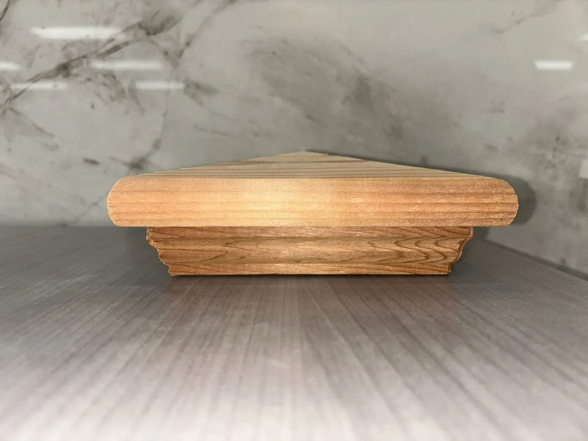 Wooden post cap with beveled edges, resting on a light-colored surface, against a marbled background.