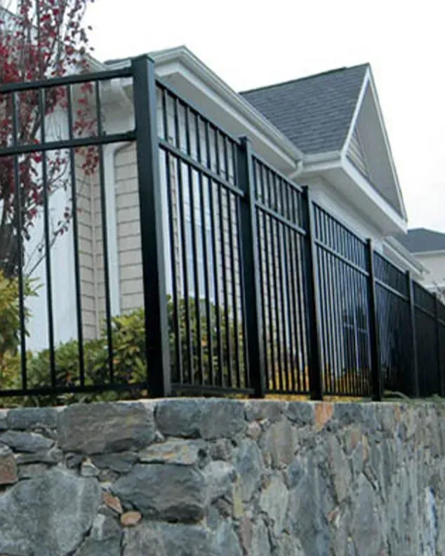 Black metal fence atop a stone wall, bordering a house with a gray roof.