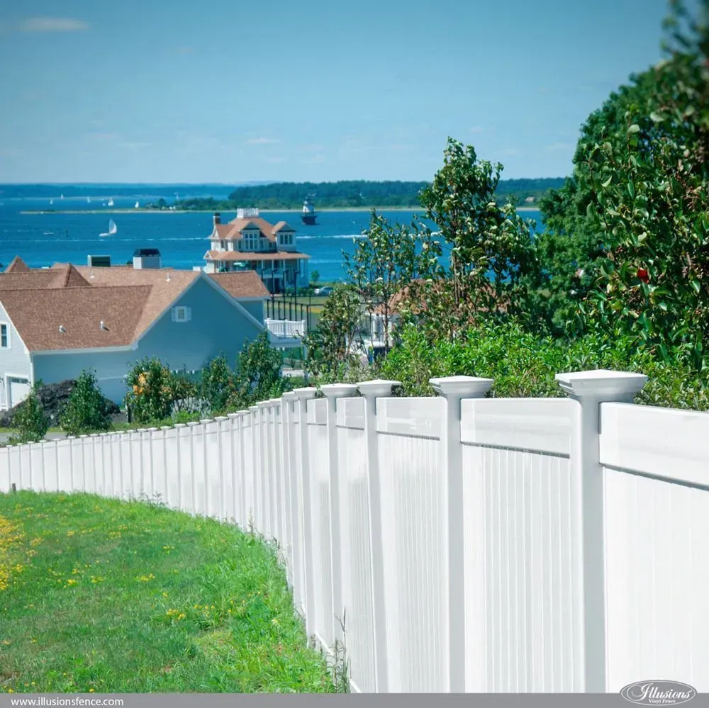 White fence overlooking a blue sea with houses and trees under a clear sky.