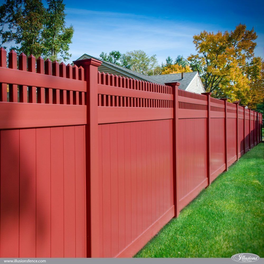 Red wooden fence in a yard, under a blue sky, with a house and trees in the background.
