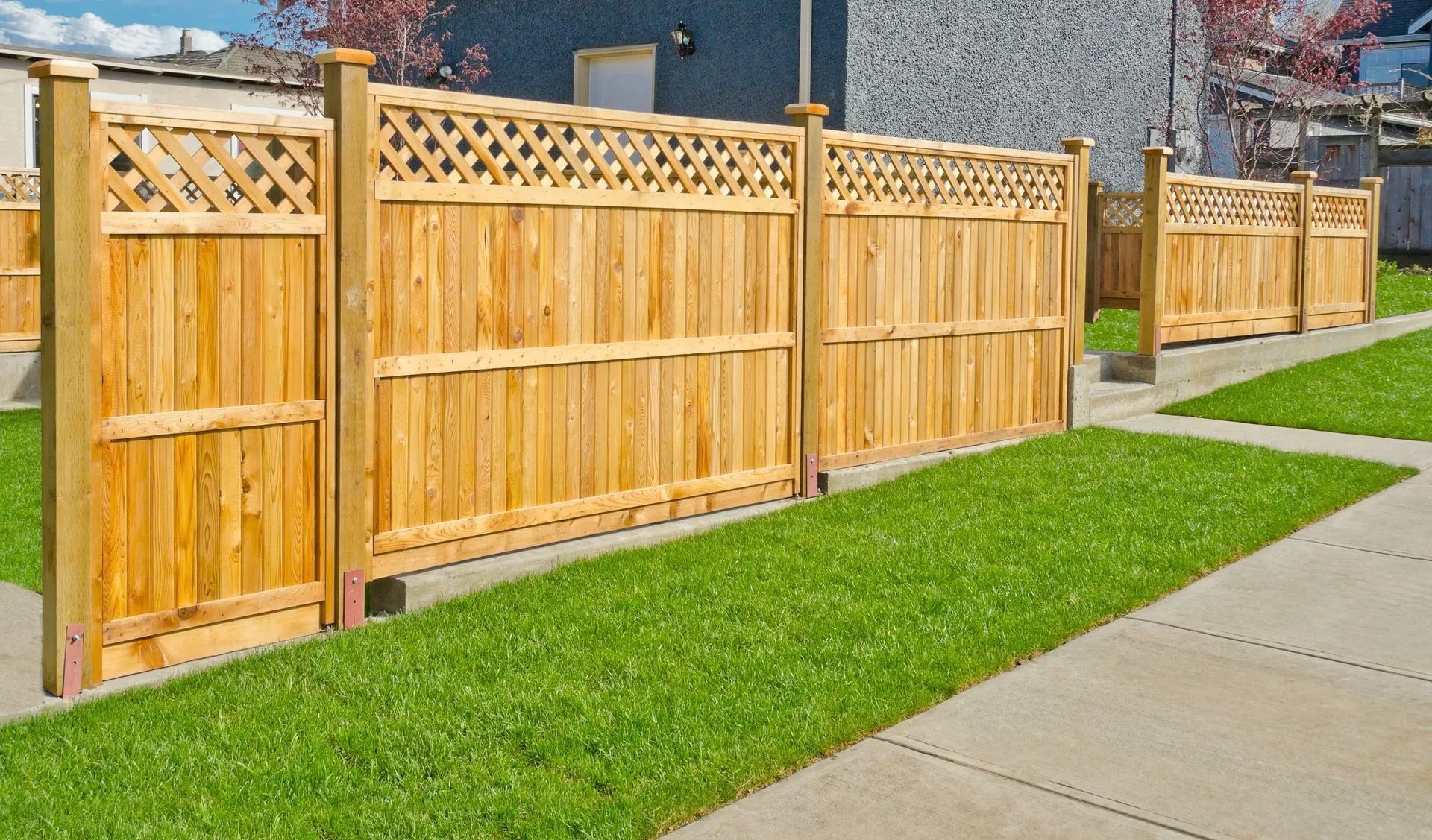Wooden fence with lattice top, along a green lawn and sidewalk.