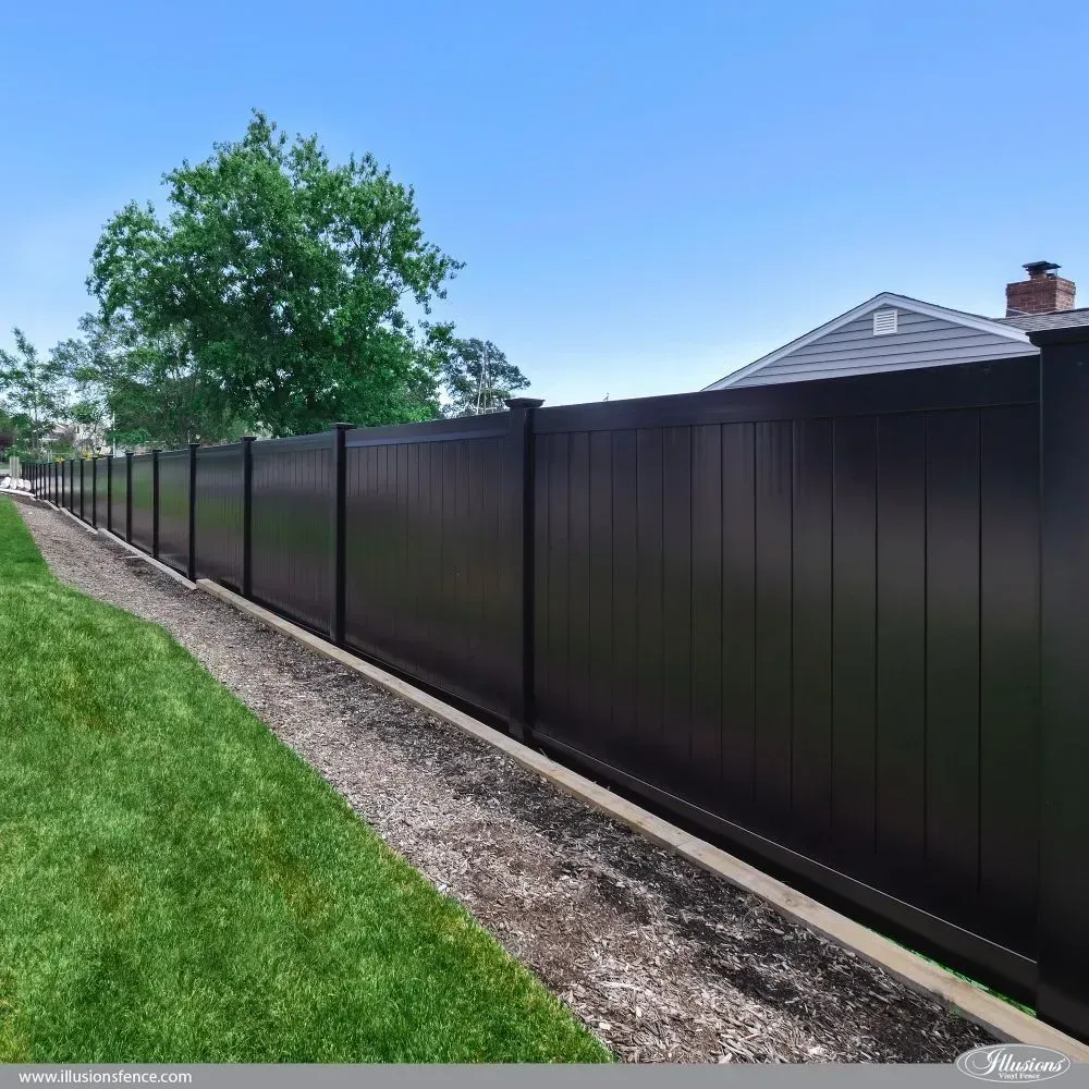 Black privacy fence along a green lawn and gravel path, under a clear blue sky.
