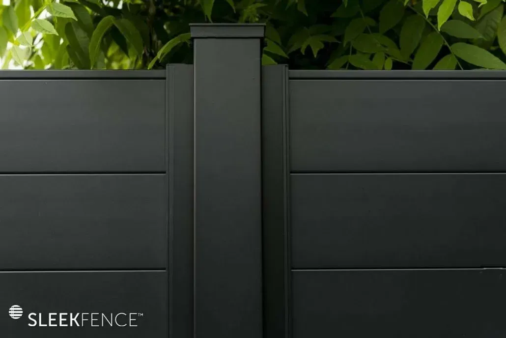 Black aluminum fence with a central post, green foliage in the background.