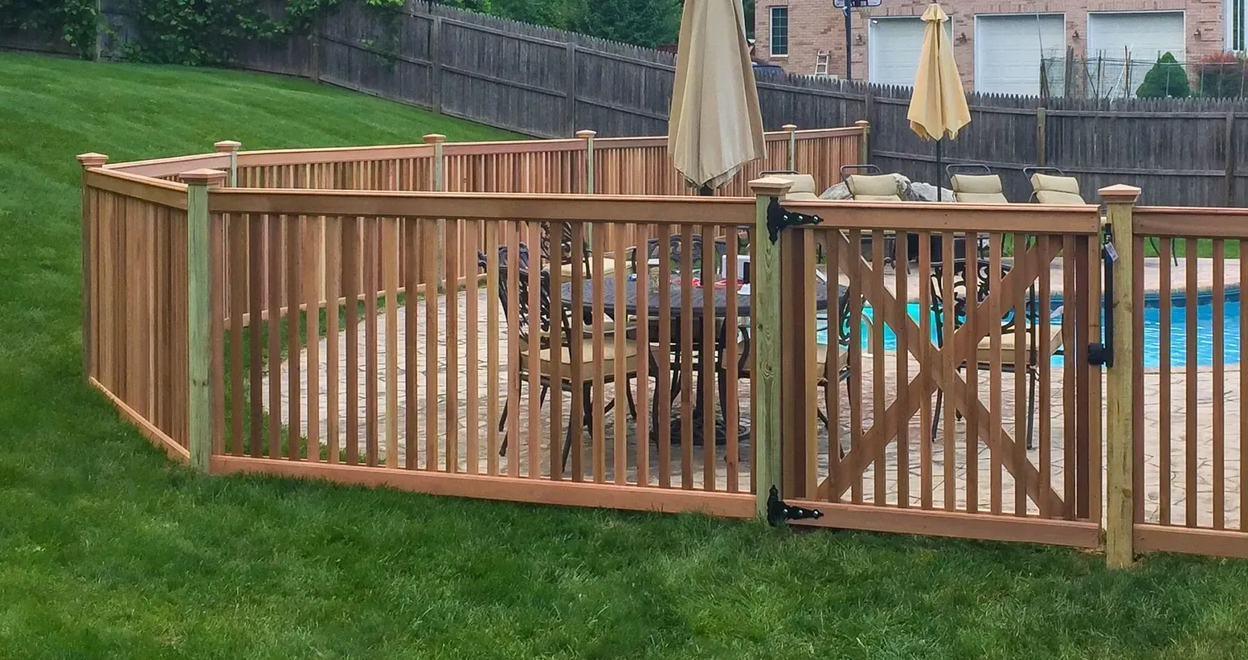 Wooden fence with a gate enclosing a pool area with patio furniture and umbrellas.