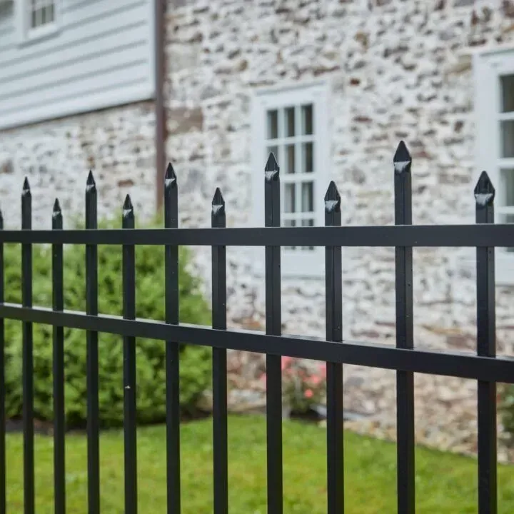 Black metal fence with pointed tops in front of a stone building with white windows.
